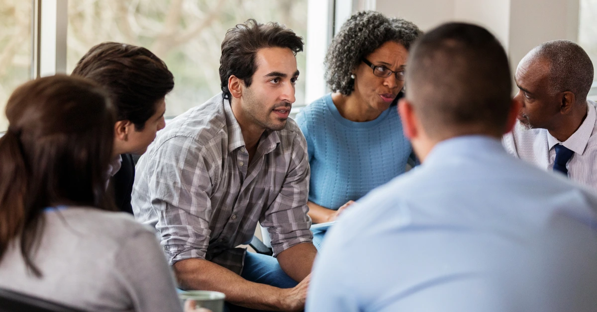 Diverse group of individuals engaged in a guided group therapy session, sharing personal experiences and offering mutual support in a safe environment